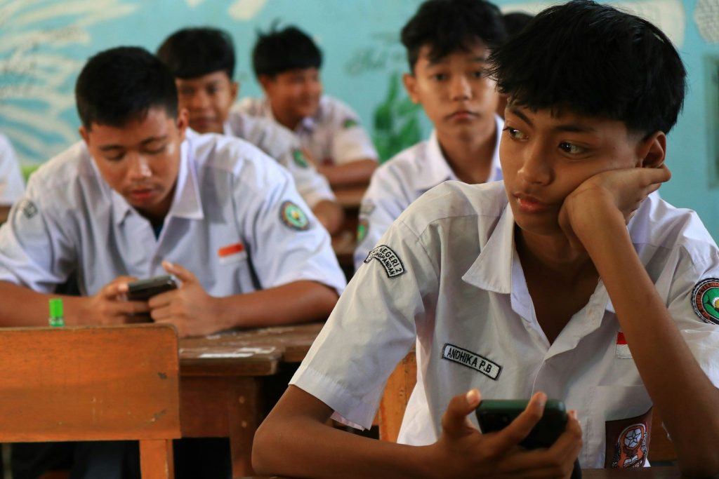 Teenage students in uniform using phones in class