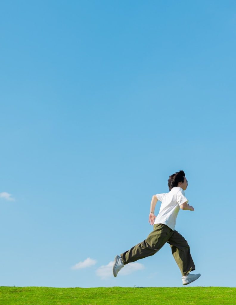 Man running on green grass under a clear blue sky