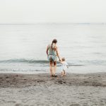 woman and baby walking on gray sand seashore during daytime