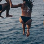 one woman and two men jumping at sea