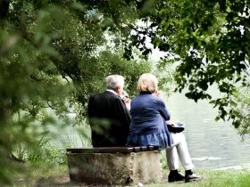 two people sitting on pavement facing on body of water