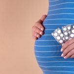 pregnant woman in blue dress holding blister pack